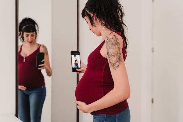 Pregnant woman stands in front of a mirror looking at her pregnancy bump.